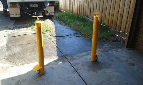 Removable bollards set into a concrete driveway beside a fence in Bayswater
