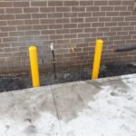 Two yellow bollards protecting a gas meter against a brick wall