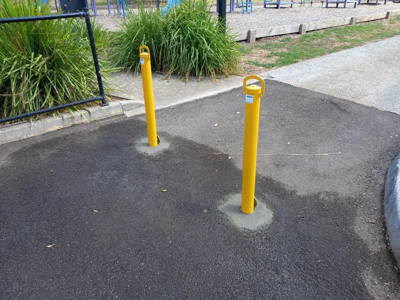 Two removable bollards blocking vehicle access to a path beside a park